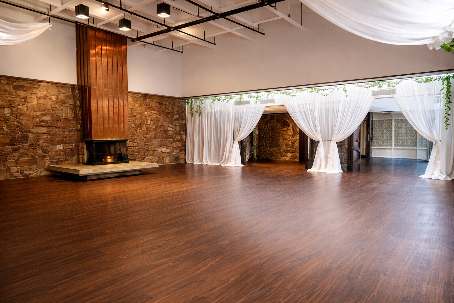 Fireside Room with rustic stone walls, wood flooring, white drapery, and a tall central fireplace