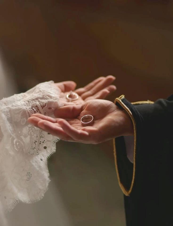 Two hands holding wedding rings above a soft neutral background
