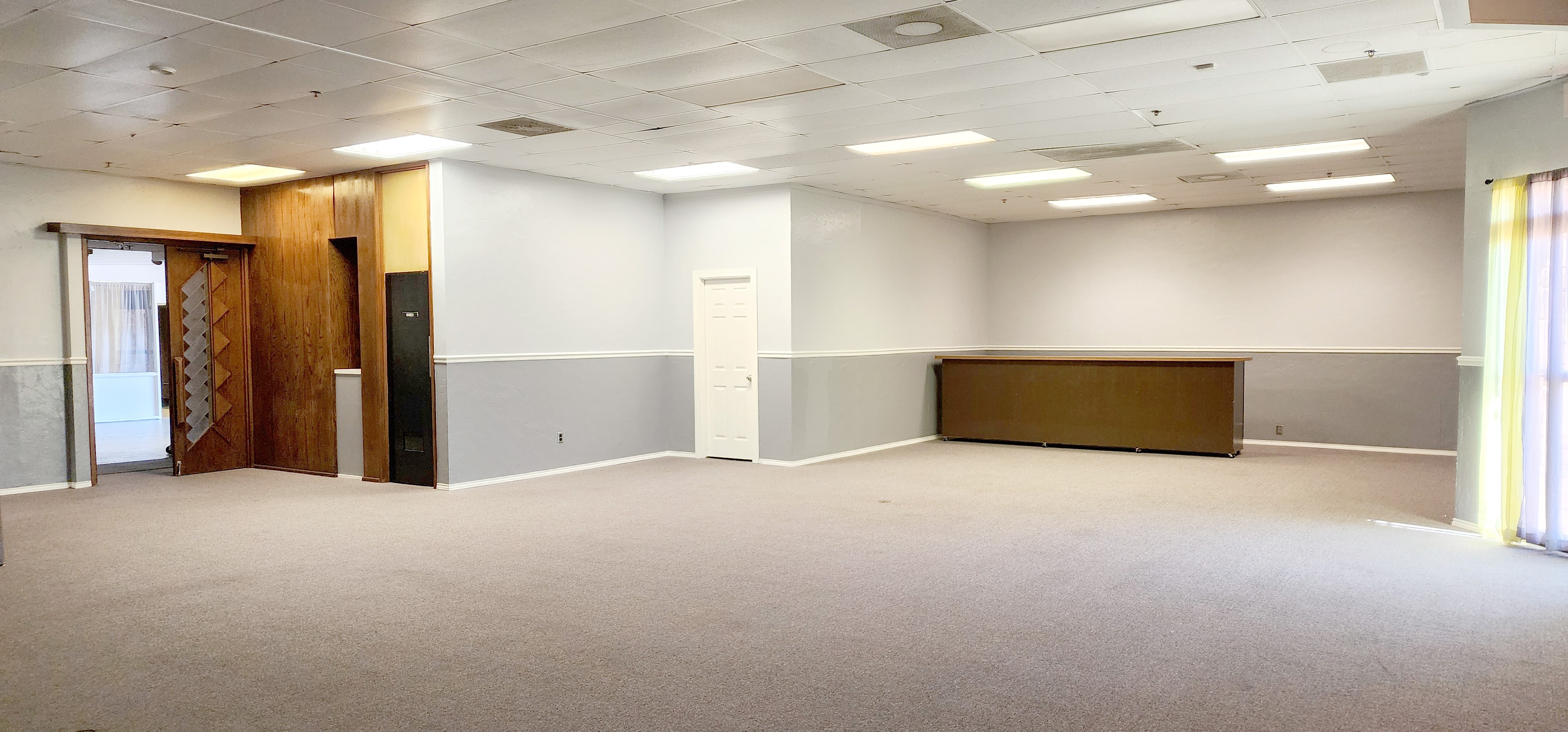 Intimate gathering space with open floor area, soft neutral walls, and a bar setup along the back wall