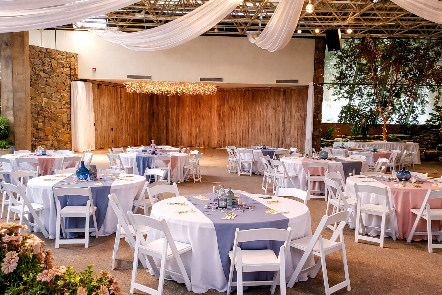 Rock Garden Room set for an elegant wedding reception with draped ceiling fabric, wood backdrop, and round tables